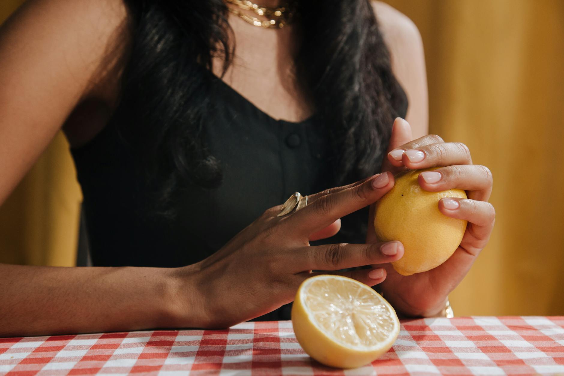 A hand with white nails holding a lemon on a soft pink background, representing the refreshing sensitivity reset that lemon vibrators can offer