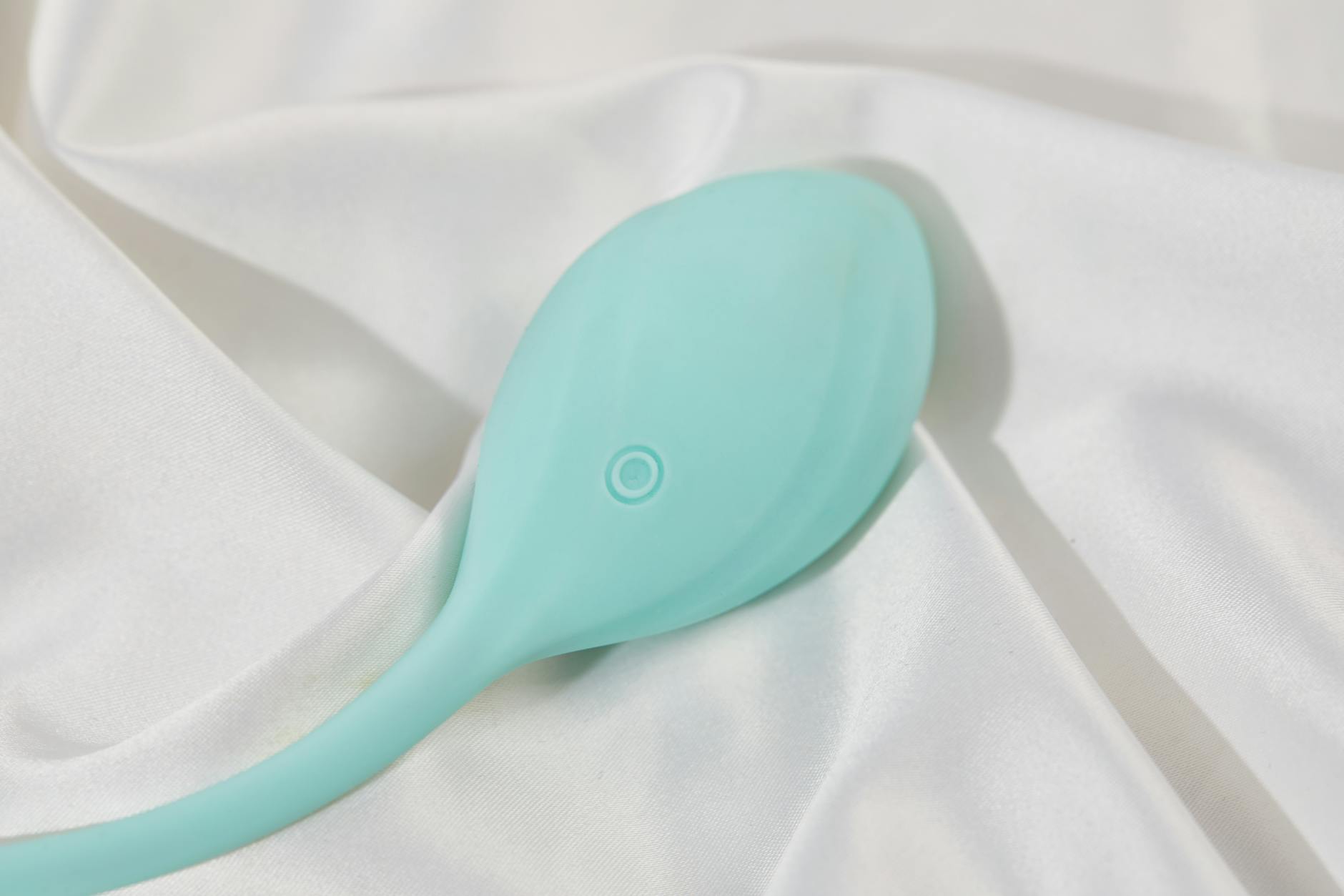 Vibrador color azul teal sobre tela de seda blanca y lisa, perfecto para imágenes de estilo de vida para adultos.