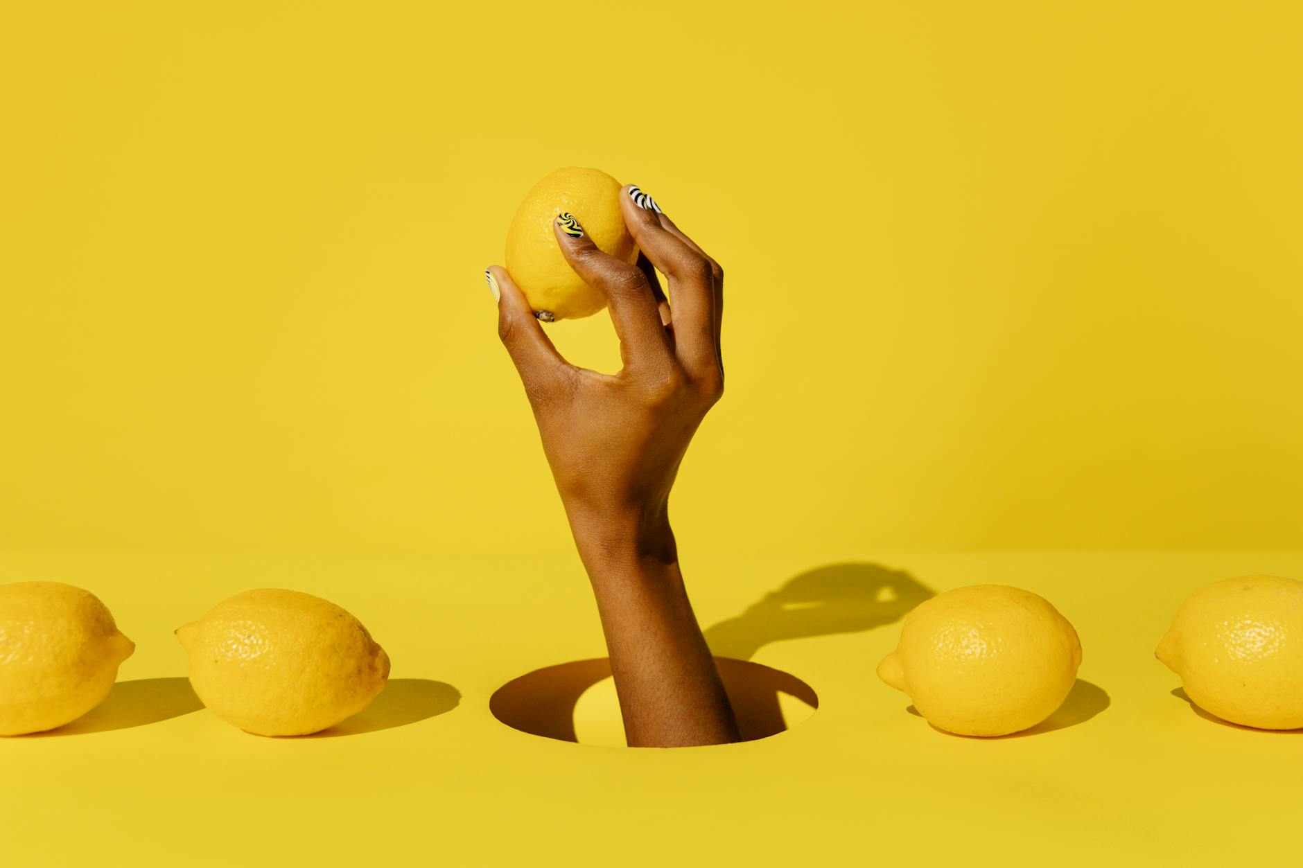 A hand holding a fresh lemon against a vivid yellow background, representing brightness and renewed sensation.