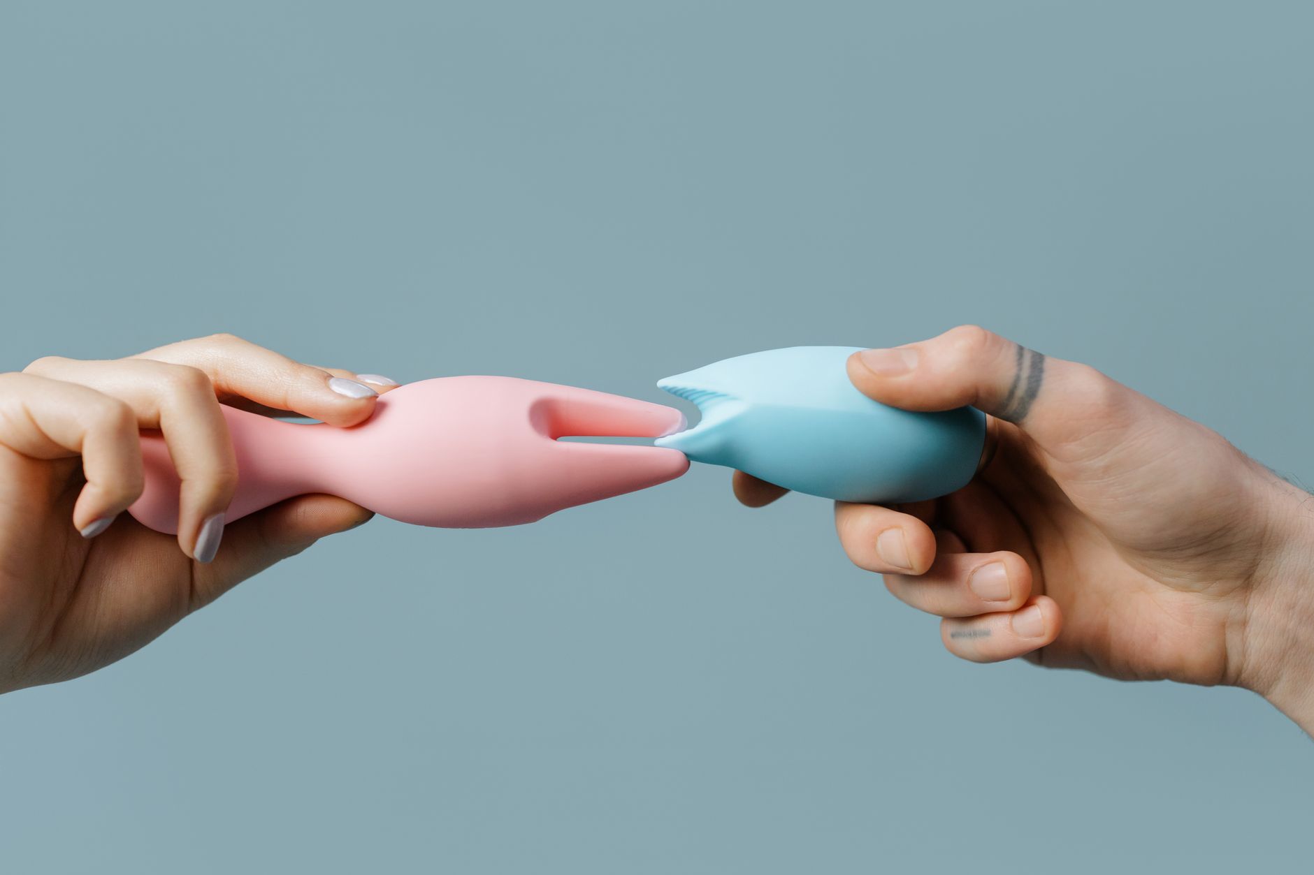 Two hands holding colorful silicone toys against a white surface, representing shared pleasure and couples exploration.