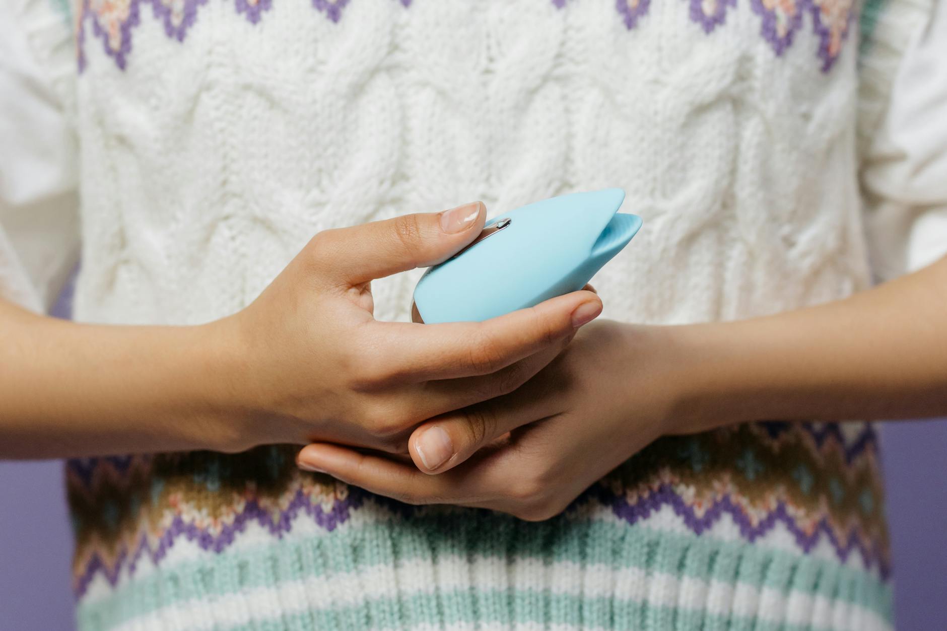 Hands holding a blue clitoral vibrator against a cozy knitted sweater