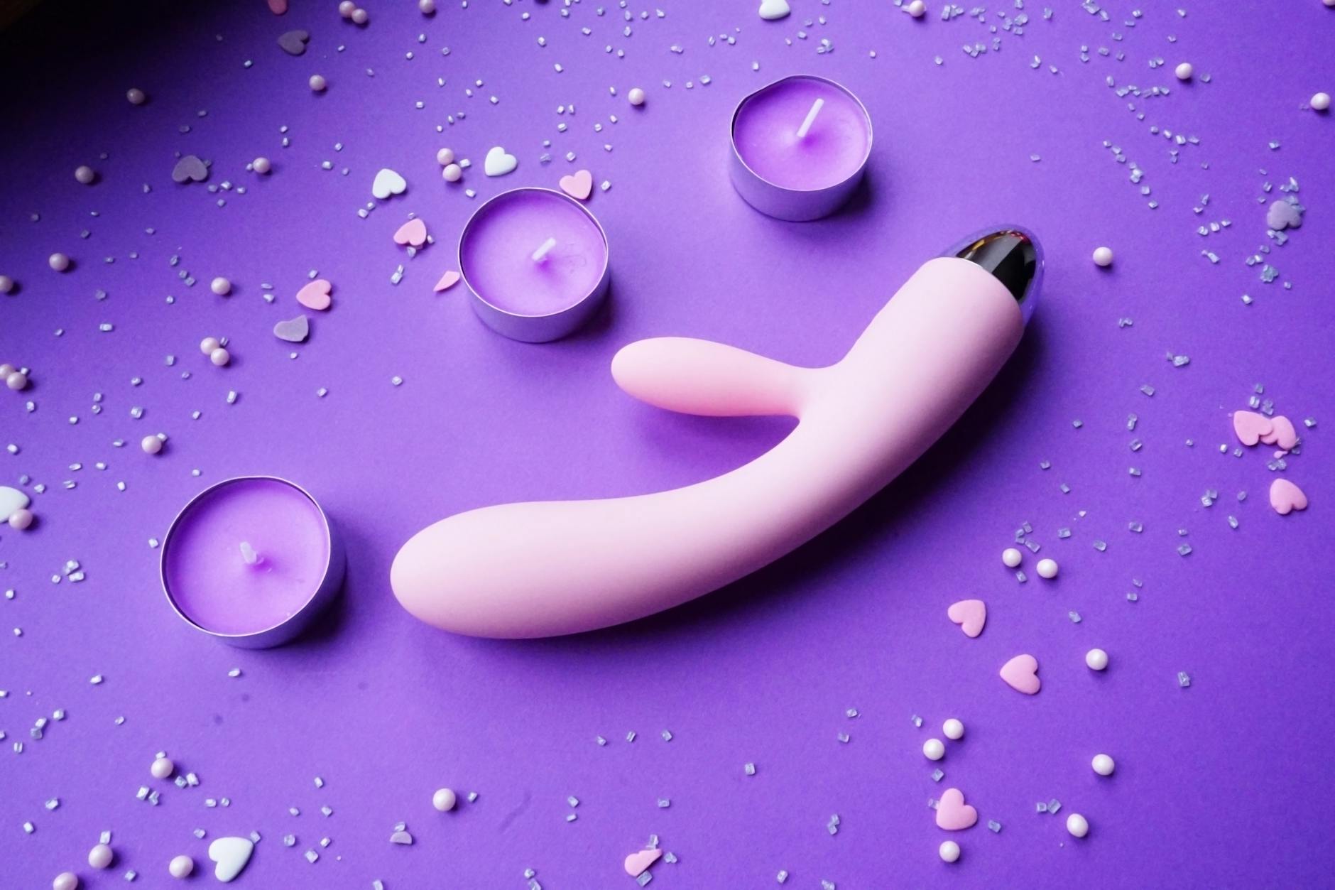 Pink lemon clitoral vibrator on a purple background with heart confetti and candles for a romantic vibe